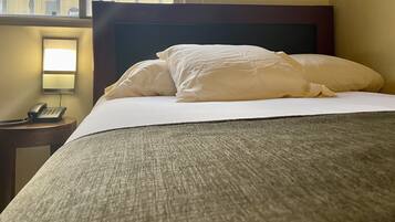 A hotel room with a neatly made bed, a bedside telephone, and a lamp on a nightstand.