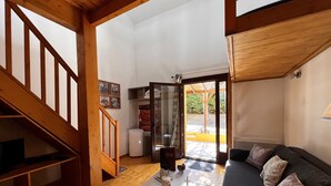 Un salón espacioso con una escalera de madera, un sofá con cojines estampados y un ventanal que da al exterior.