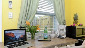 A laptop on a table with a window, curtains, a coffee maker, a bottle, and a pineapple on the windowsill. - Siesta Palms (sarasota)