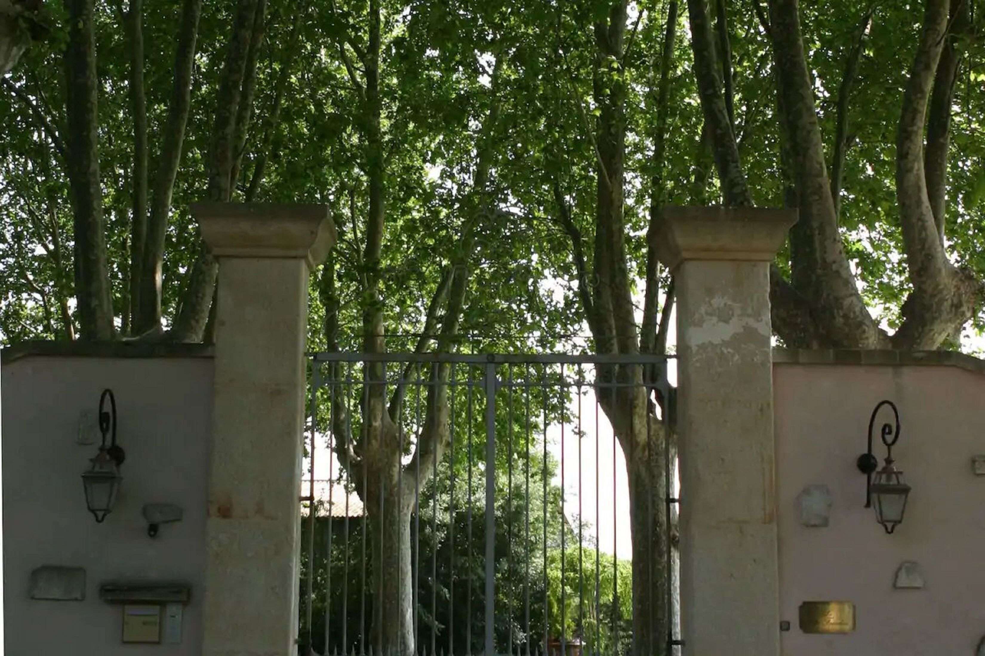 A gated entrance with a metal gate, stone pillars, and wall-mounted lanterns.