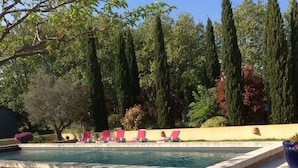 A swimming pool with pink lounge chairs and tall trees in the background. - Mas Petit Fourchon (Arles)