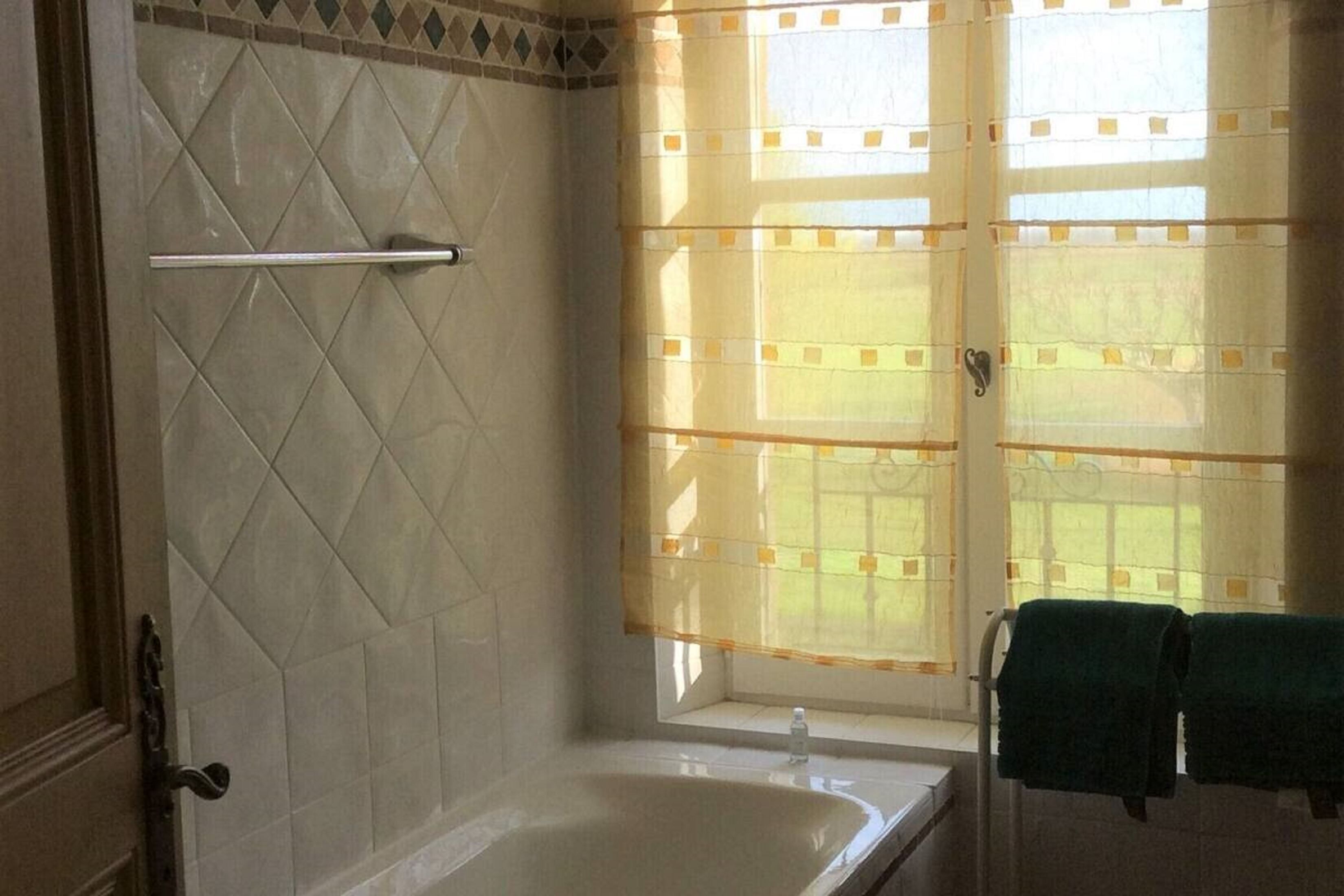 A bathroom with a bathtub, a towel rack with two towels, and a window with a patterned curtain.