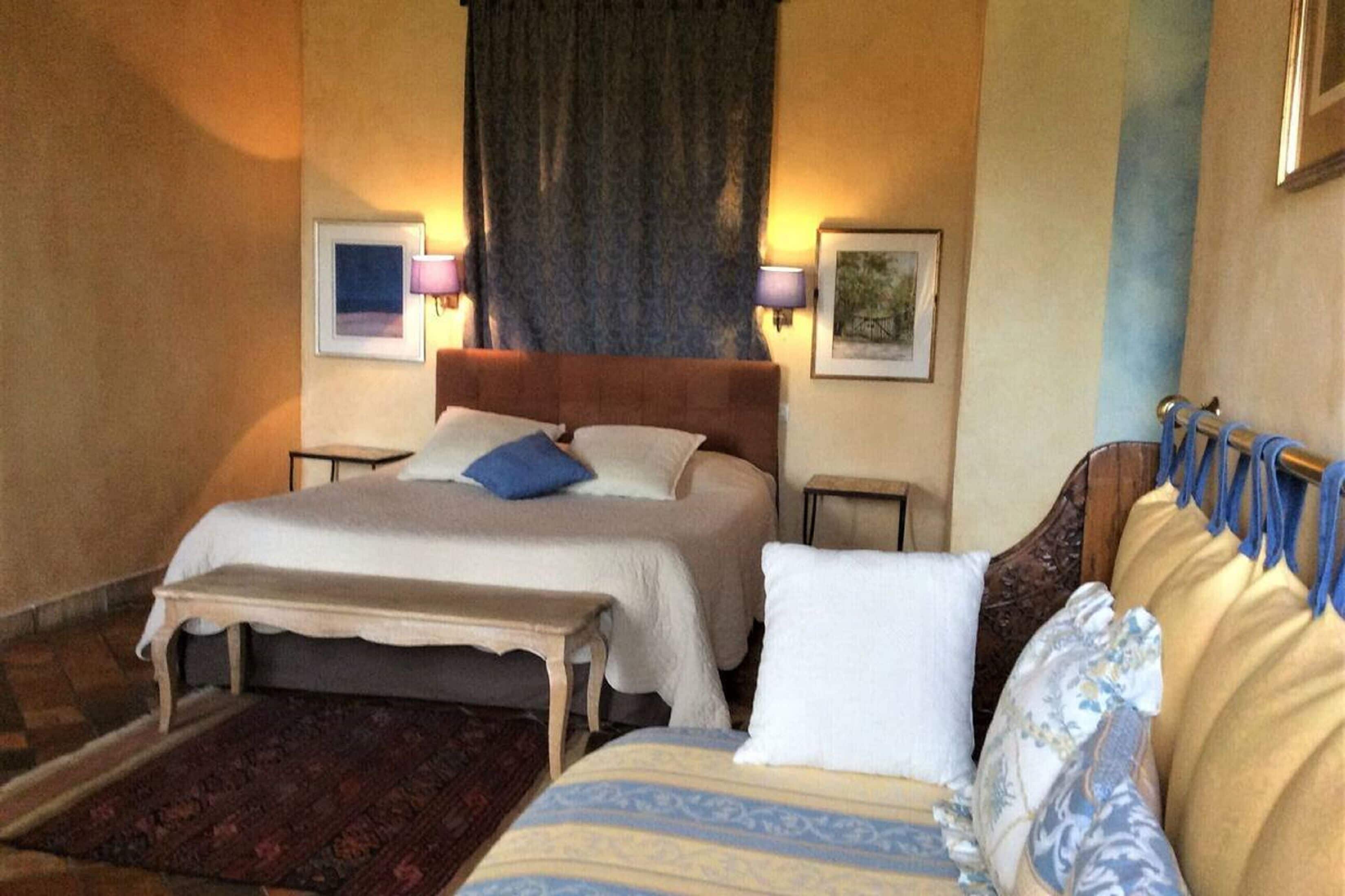 A double bed with a wooden headboard, a bedside table, and a bench. There are two wall-mounted lamps and framed pictures on the walls.