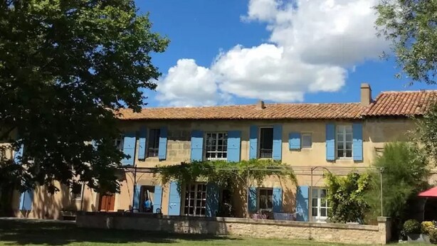 A two-story building with a tiled roof, blue shutters, and a stone facade. - Mas Petit Fourchon (Arles)