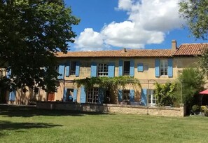 A two-story building with a tiled roof, blue shutters, and a stone facade. - Mas Petit Fourchon (Arles)