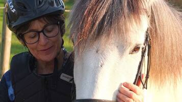 Una persona con casco y chaleco con identificación, acariciando un caballo blanco con brida.