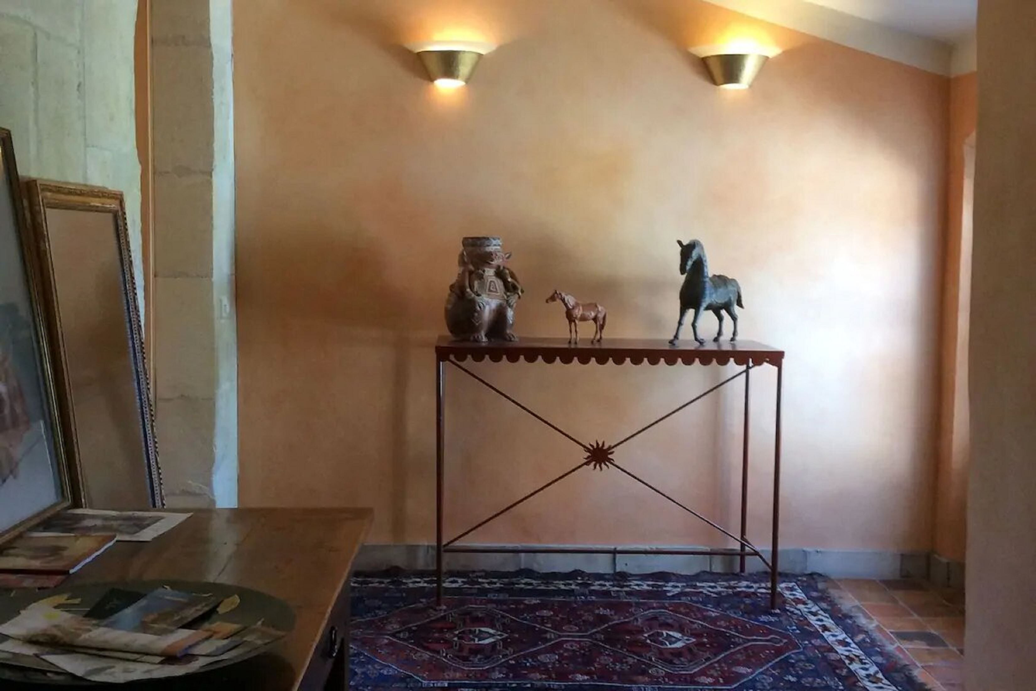 A room with a patterned rug, a metal console table with decorative items, and wall-mounted lighting.