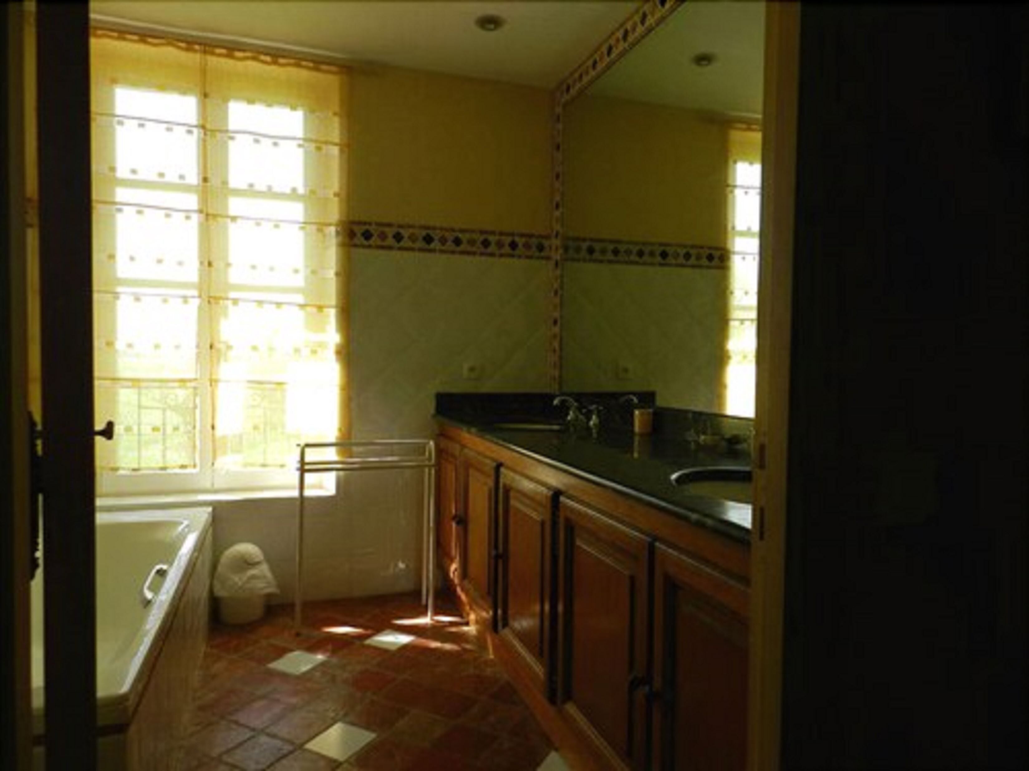 Un baño con bañera, lavabo y ventana con cortinas.