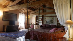 A bedroom with a large bed, wooden beams, a television, a bookshelf, and a painting on the wall. - Mas Petit Fourchon (Arles)