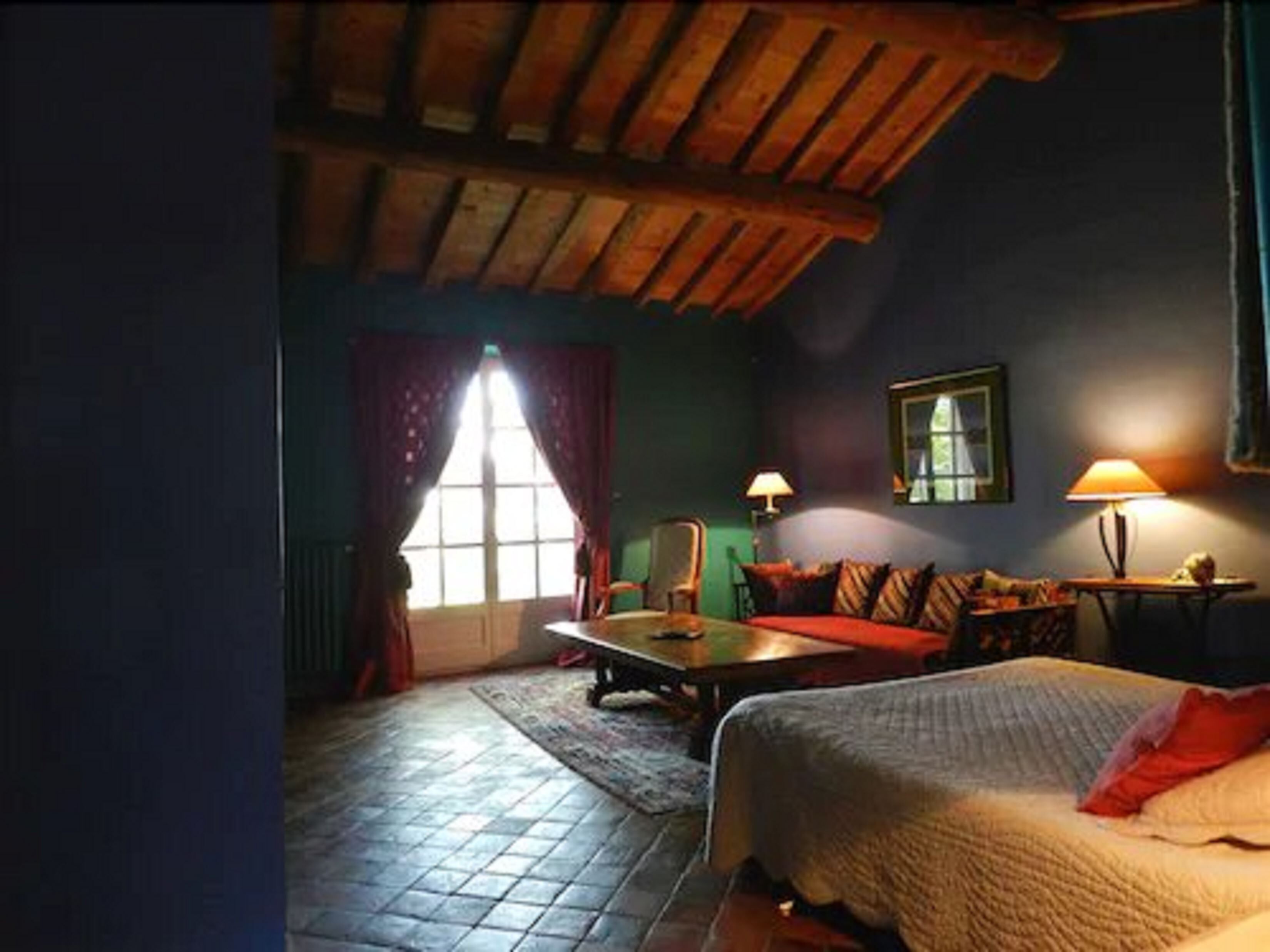 Una camera accogliente con soffitto spiovente, un letto con cuscino rosso, un tavolo e due lampade.