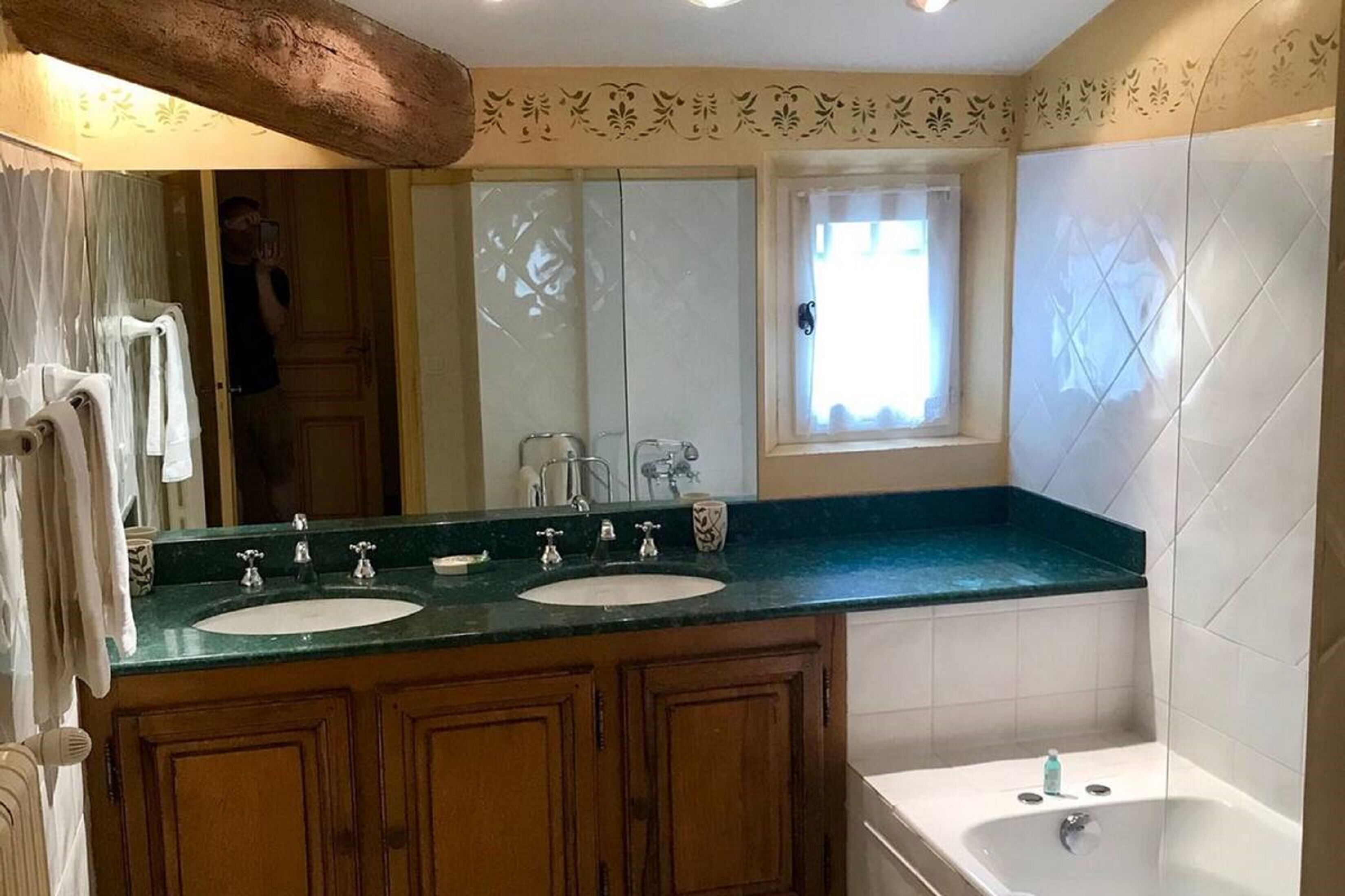 A bathroom with two sinks, a bathtub, and a window with curtains.