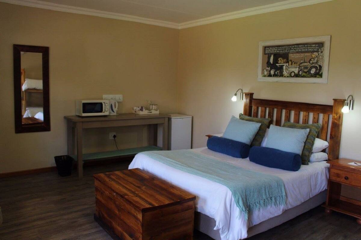 Ein Schlafzimmer mit einem Bett, Nachttischen, einer hölzernen Bank, einem Schreibtisch mit einer Mikrowelle und einem Wandbild.