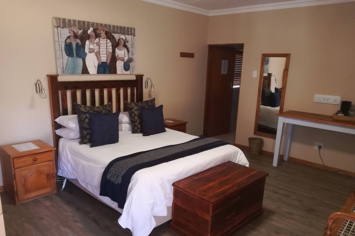 Ein Schlafzimmer mit einem großen Bett, einem Holzkopfteil, einem Nachttisch, einer Bank, einem Schreibtisch und einem Spiegel.