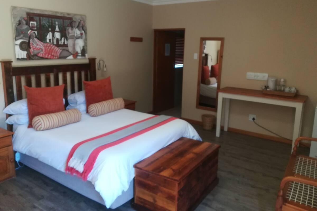 Ein Schlafzimmer mit Bett, Holz-Kopfteil, Nachttischen, einem Spiegel, einem Schreibtisch und einem Bild an der Wand.