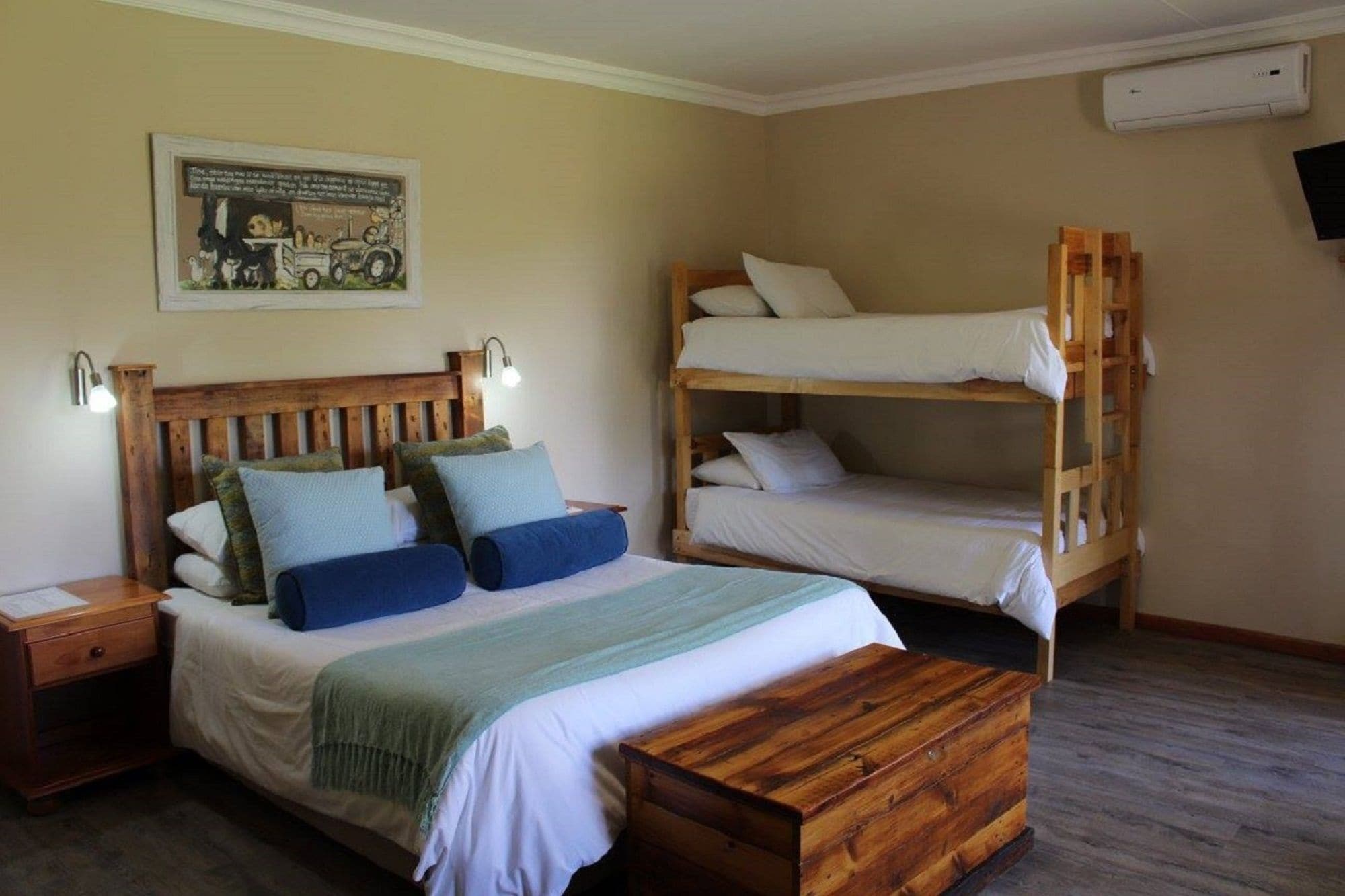 A bedroom with a bunk bed, a single bed with pillows and a blanket, a wooden nightstand, and a wall-mounted air conditioner.