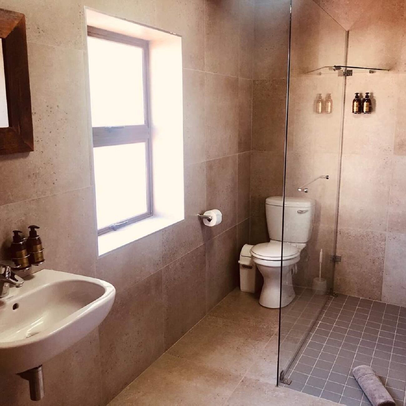 A bathroom with a sink, toilet, and shower. There is a window providing natural light.
