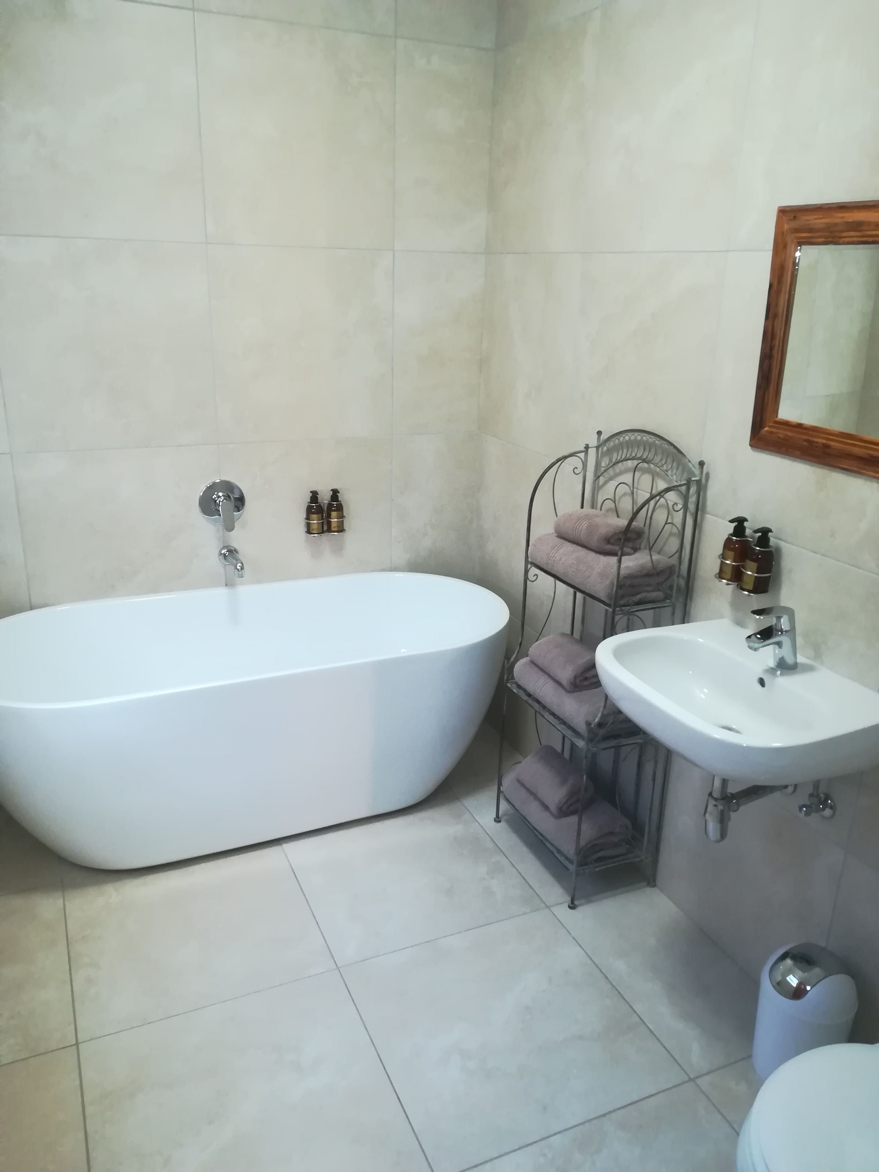 Une salle de bain avec une baignoire blanche, un lavabo et une étagère en métal où sont posées des serviettes.