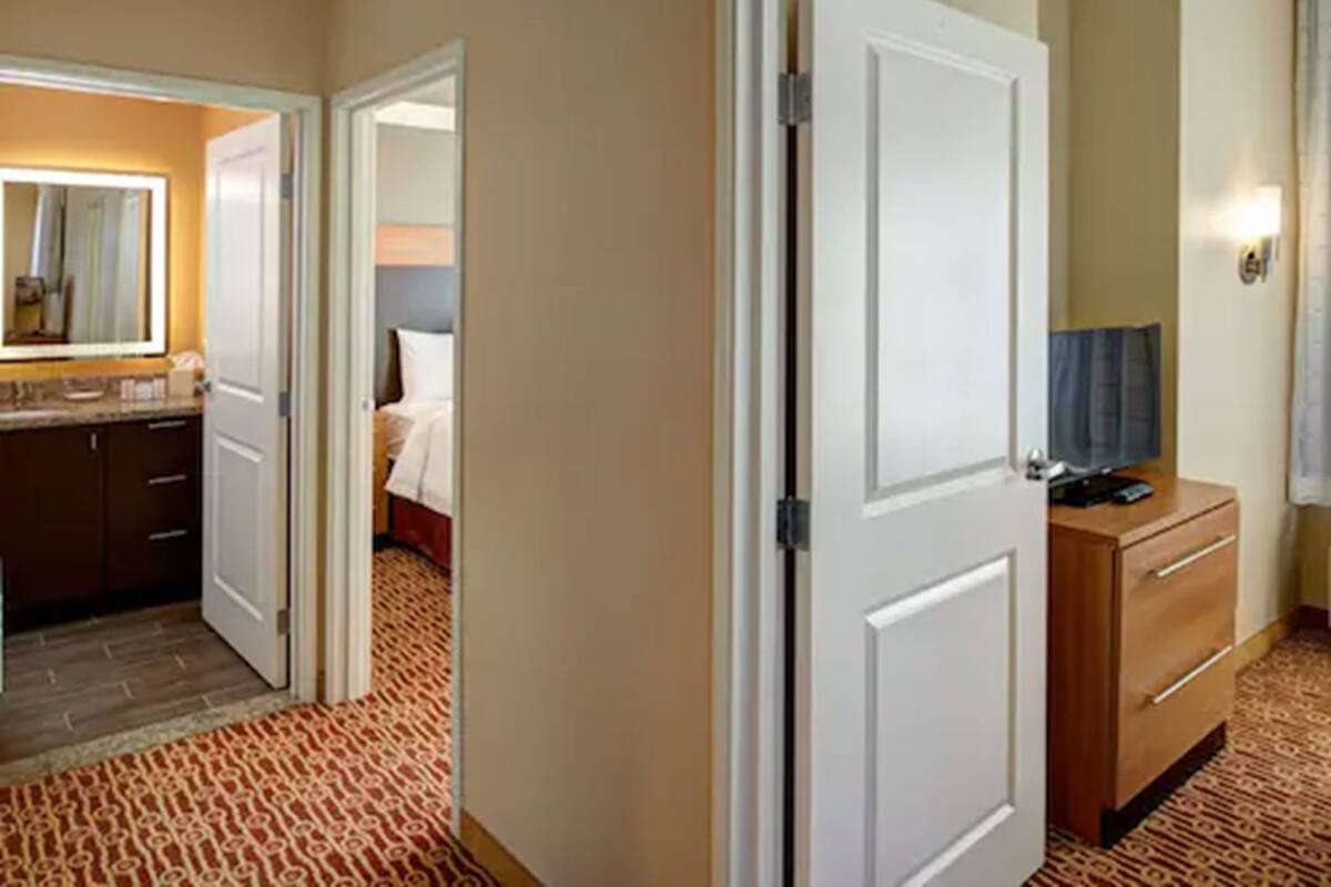 A hotel room with a bed, a dresser, a television, and a bathroom with a mirror and sink.