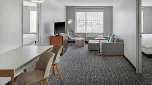 Habitación de hotel con escritorio, dos sillas, sofá, televisión y una ventana grande con vistas a la ciudad.