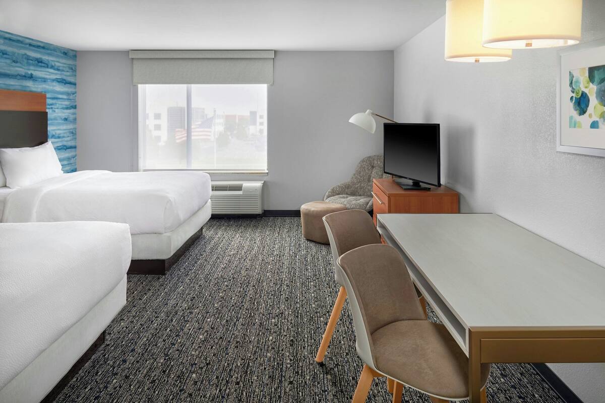 A hotel room with two beds, a desk, a television, and a window with a city view.