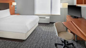 Una habitación de hotel con una cama grande, un escritorio con silla, televisor y ventana con persianas.