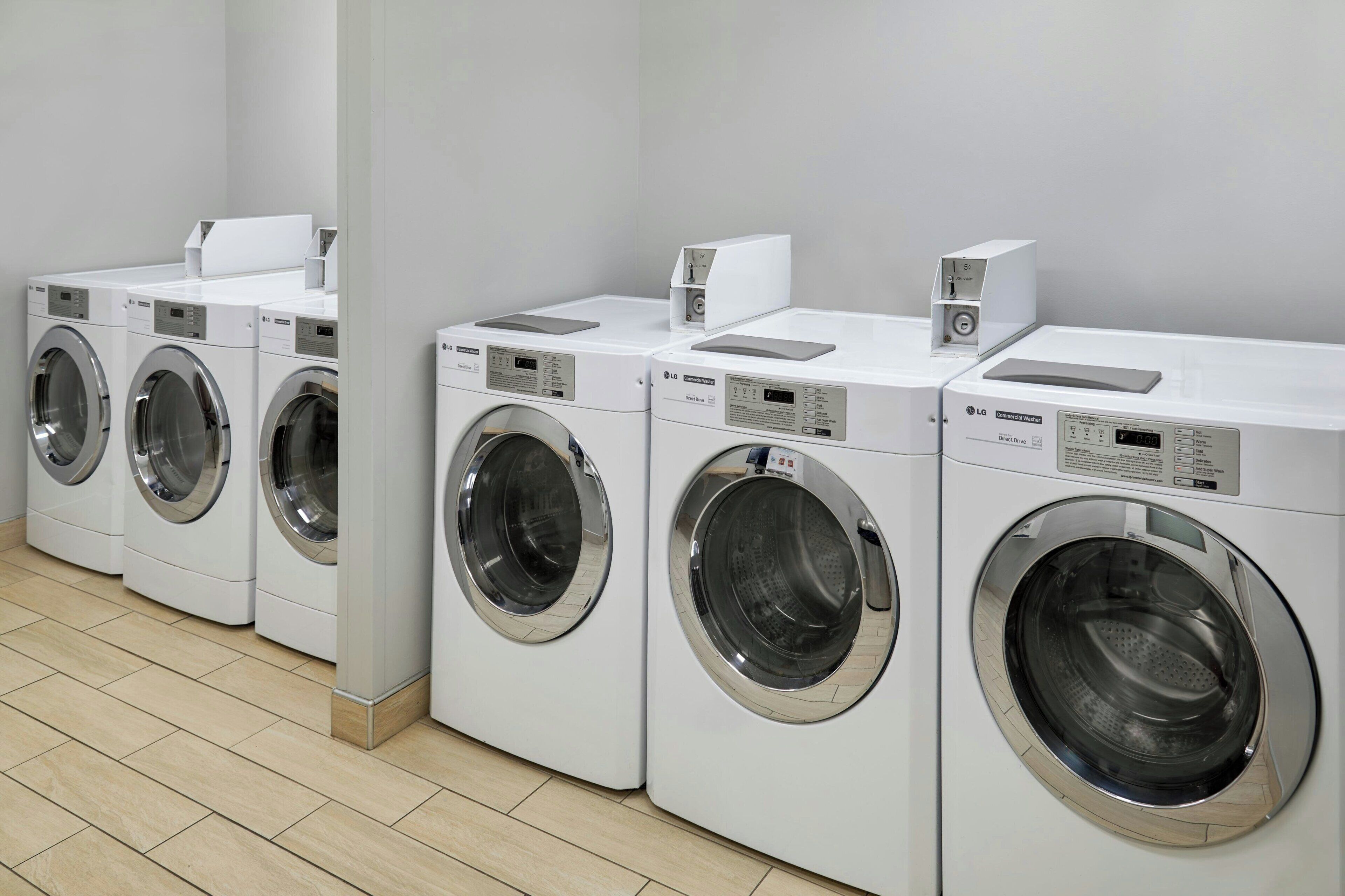 A row of white front-loading washing machines in a clean, tiled room.