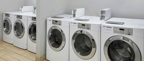 A row of white front-loading washing machines in a clean, tiled room.