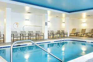 A swimming pool with a blue tiled edge, surrounded by lounge chairs and a tiled floor.