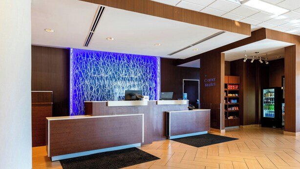 A hotel reception area with a blue-lit wall, a reception desk, a vending machine, and a sign for the 'Curry Market.' - Fairfield Inn & Suites Richmond Midlothian (Richmond)
