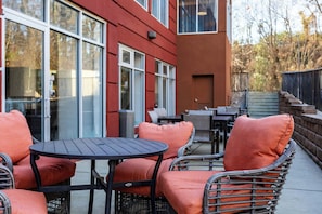 An outdoor seating area with wicker furniture and orange cushions, a red building with large windows, and a staircase leading to a higher level.