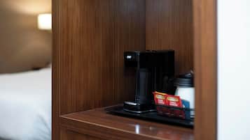 A wooden bedside table with a coffee maker and a cup of coffee, a tray with a packet of sugar and a small container.