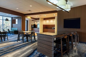 A modern hotel lobby with a bar area, seating arrangements, and a large TV screen.