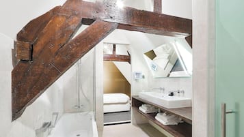 Un baño moderno con una viga de madera en el techo, una bañera, un lavabo y un espejo.