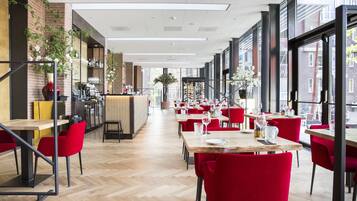 A modern restaurant with red chairs, wooden tables, and large windows offering a view of the street.