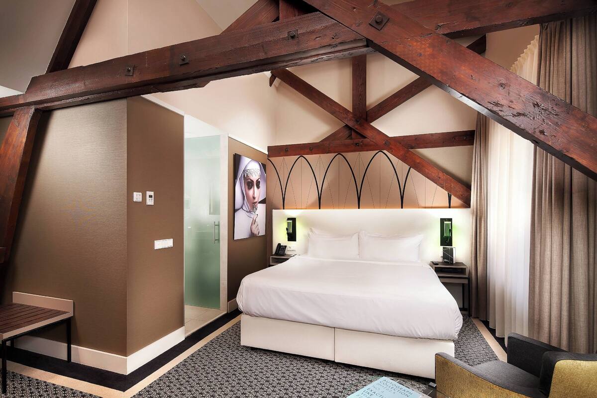A hotel room with a large bed, wooden beams, a desk, and a chair.