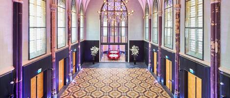 A grand hallway with arched windows, a patterned floor, and a chandelier.