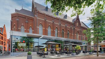 Un edificio histórico con una extensión de vidrio moderna que alberga un restaurante y mesas al aire libre.