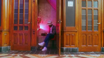 A person sitting on a bench in a doorway with ornate wooden doors and a tiled floor with a geometric pattern.