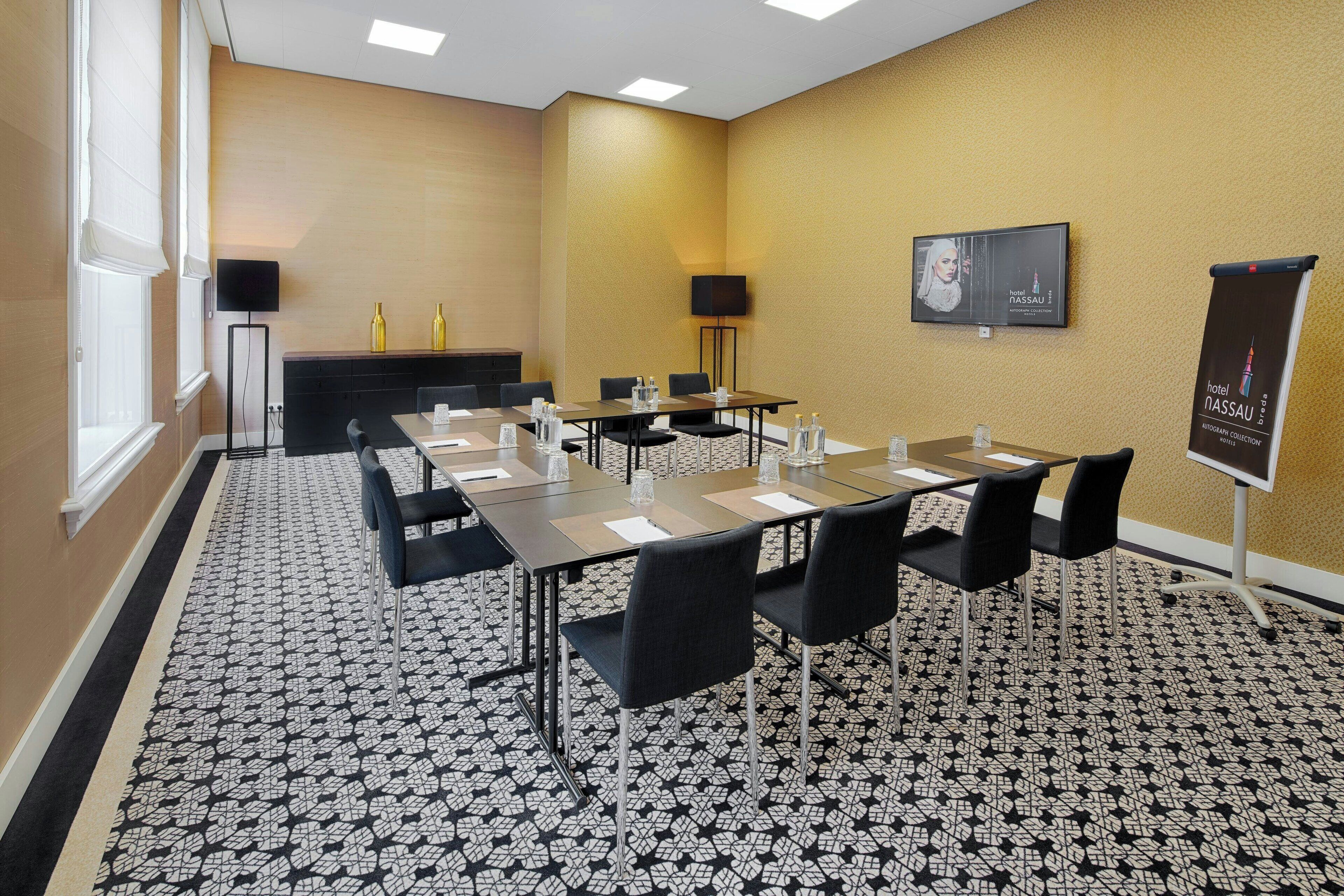 A conference room with a long table, chairs, a projector screen, and a banner.