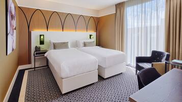 A hotel room with two beds, a desk, a chair, and a large window with curtains.