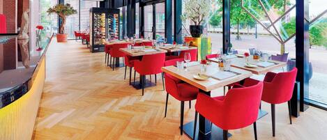 A modern restaurant with wooden flooring, red chairs, and large windows offering an outdoor view.