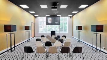 A conference room with a patterned carpet, rows of chairs, a large screen, and speakers.