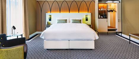 A hotel room with a large bed, a desk, a chair, and a wardrobe.