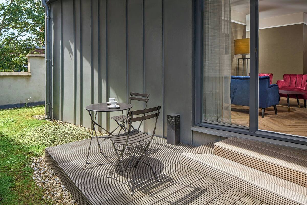 An outdoor patio with a table and chairs, a wooden deck, and a view into the interior through a glass door.