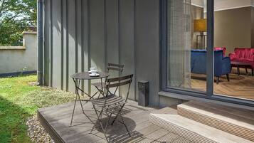 An outdoor patio with a table and chairs, a wooden deck, and a view into the interior through a glass door.