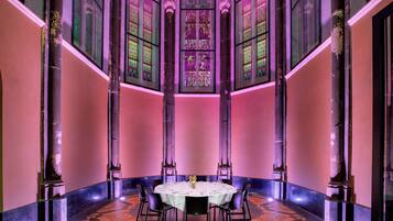 A dining area with a round table set for six, flanked by tall columns, and large stained glass windows above.