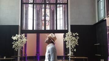 A person standing in a room with a large arched window, patterned floor, and a chandelier.