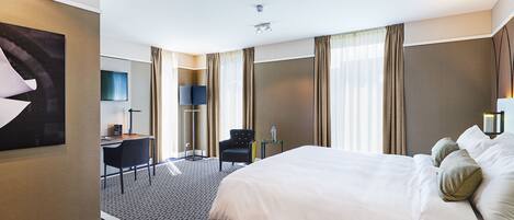 A hotel room with a large bed, a desk with a chair, a TV, and a window with curtains.