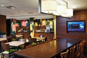 Un restaurante con mesas y sillas de madera, una zona de bar y un televisor que muestra información meteorológica.