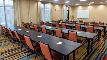 Une salle de conférence dotée de plusieurs tables et chaises, de grandes fenêtres avec des rideaux et d’un tableau blanc fixé au mur.
